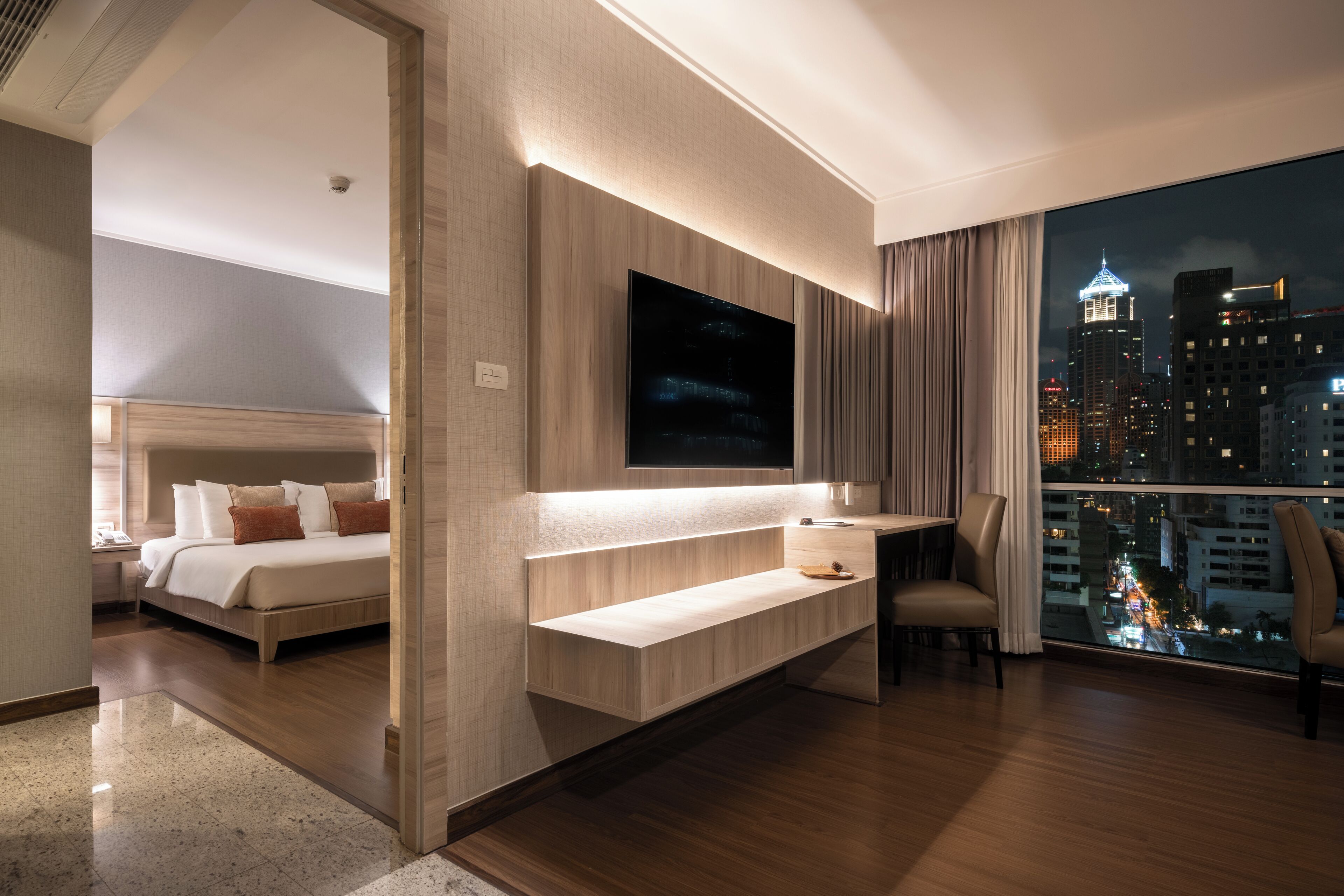 Ein modernes Hotelzimmer mit Bett, Schreibtisch, Fernseher und einem Balkon mit Blick auf die Stadt.