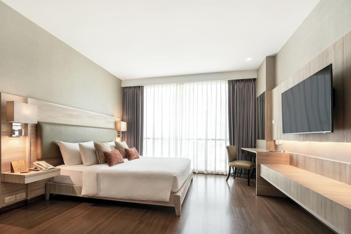 A modern hotel room with a large bed, bedside lamps, a desk, and a flat-screen TV.