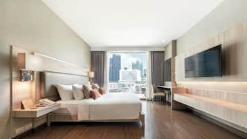 A modern hotel room with a large bed, a desk, a flat-screen TV, and a city view.