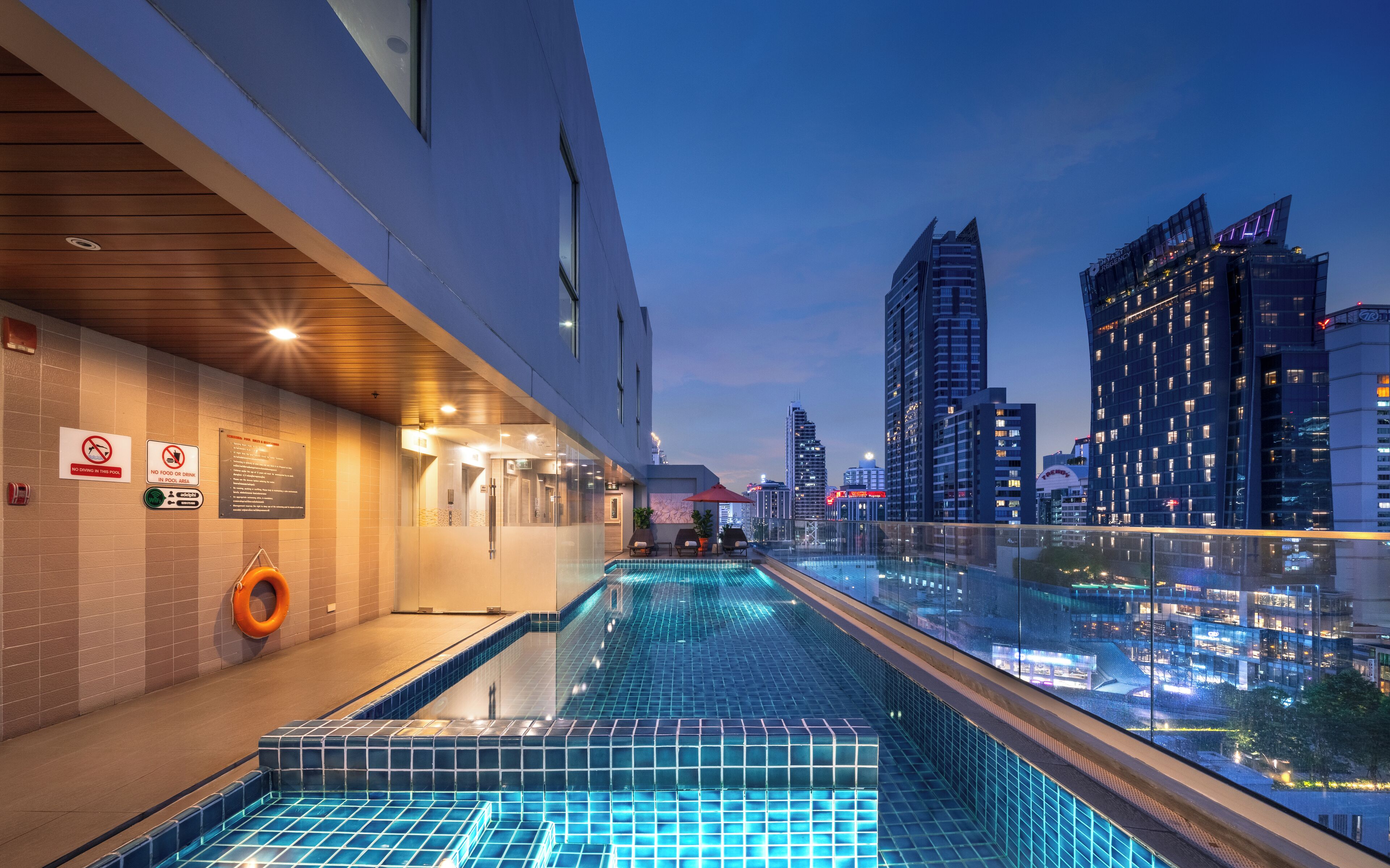 A rooftop pool with a city view, glass railings, and a no-smoking sign.