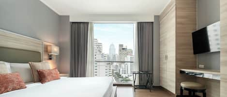 A modern hotel room with a large bed, a TV mounted on the wall, and a city view through the window.