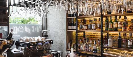 A bar area with a coffee machine, shelves of liquor bottles, and hanging wine glasses.