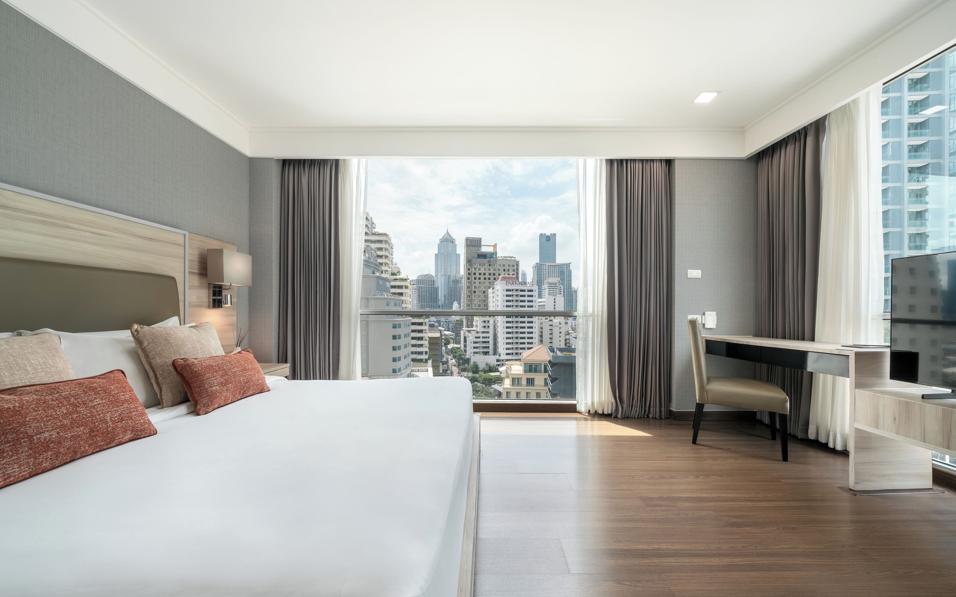 A modern hotel room with a large bed, a desk, and a view of the city skyline.