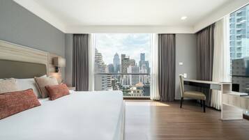 A modern hotel room with a large bed, a desk, and a view of the city skyline.