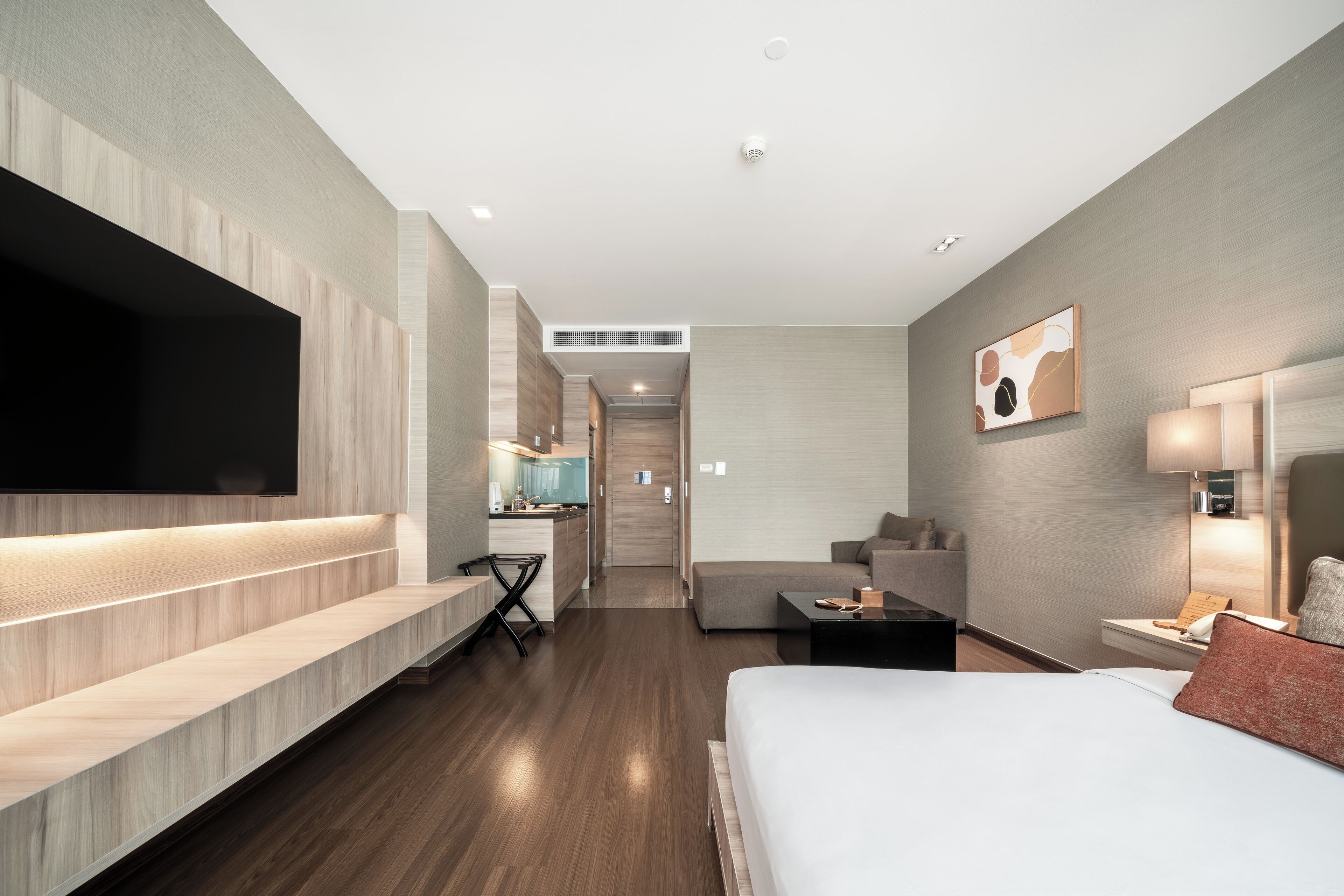 A modern hotel room with a large bed, a flat-screen TV, a desk with a chair, a sofa, and a small table.