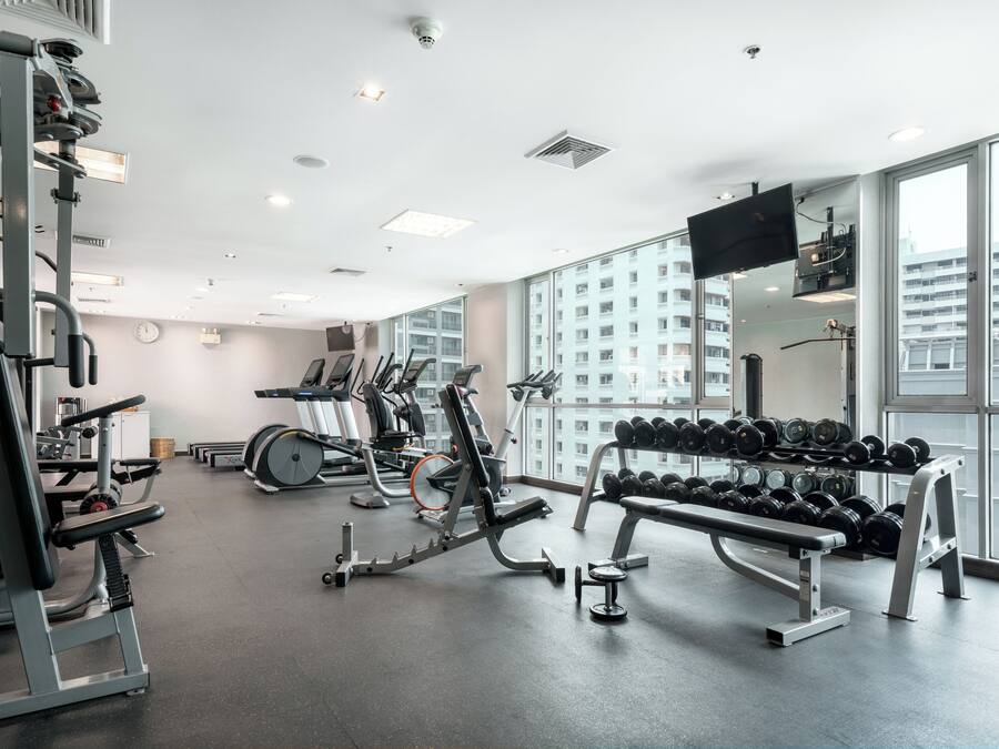 A modern gym with various exercise equipment, large windows, and a flat-screen TV.
