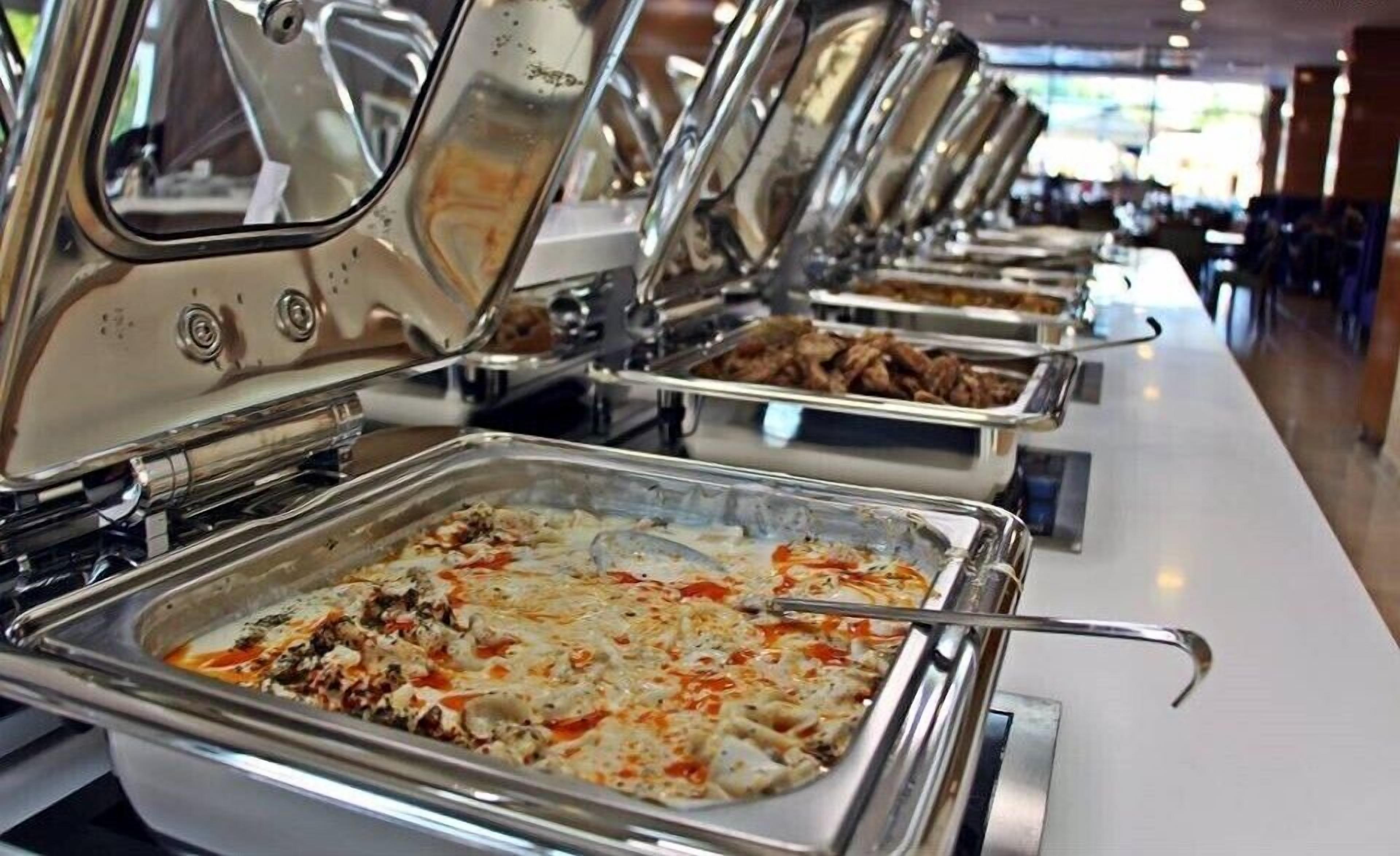 A buffet line with various dishes, including a pasta dish with cheese and tomato sauce.
