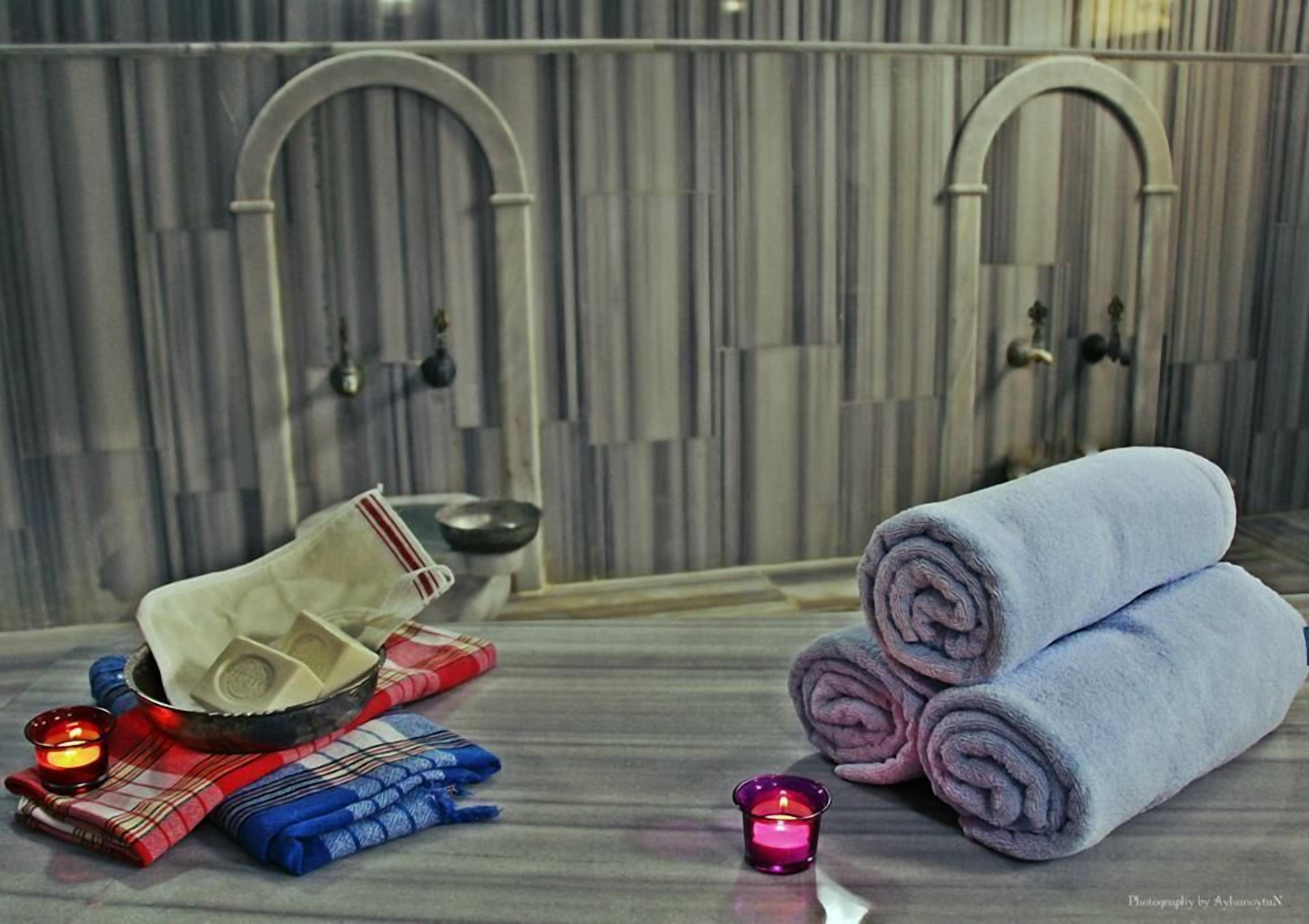 Un baño con dos lavamanos de arco, un perchero con toallas dobladas, un cuenco y una vela.