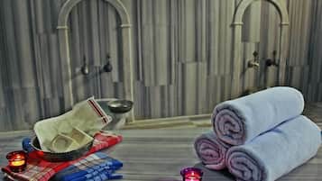 Un baño con dos lavamanos de arco, un perchero con toallas dobladas, un cuenco y una vela.