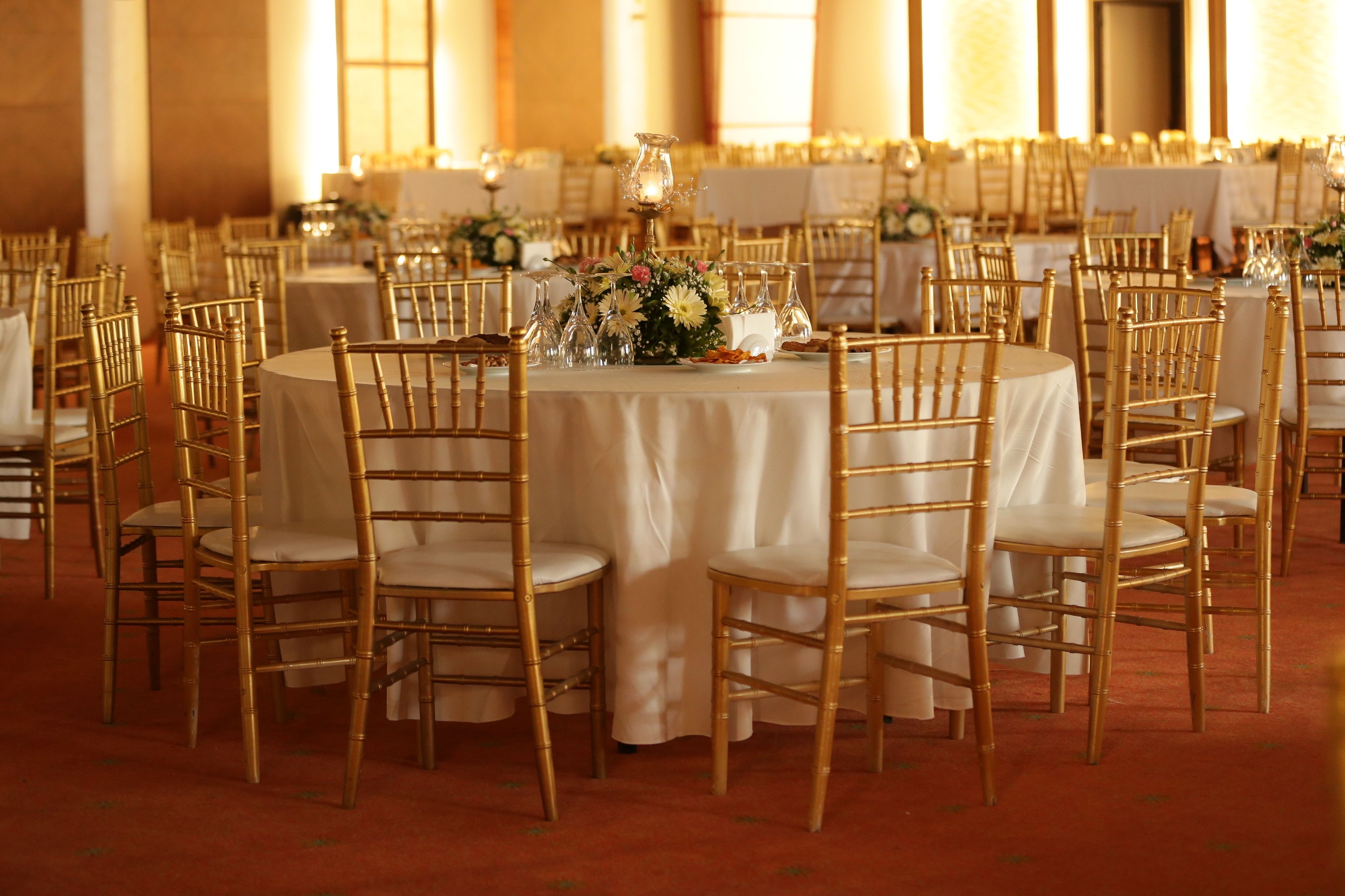A banquet hall with round tables, gold chairs, and white tablecloths.