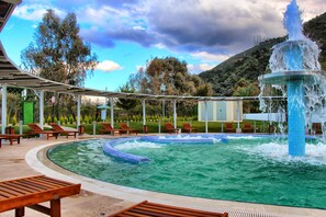 Un área de piscina con un jacuzzi circular, sillas de descanso y una fuente.