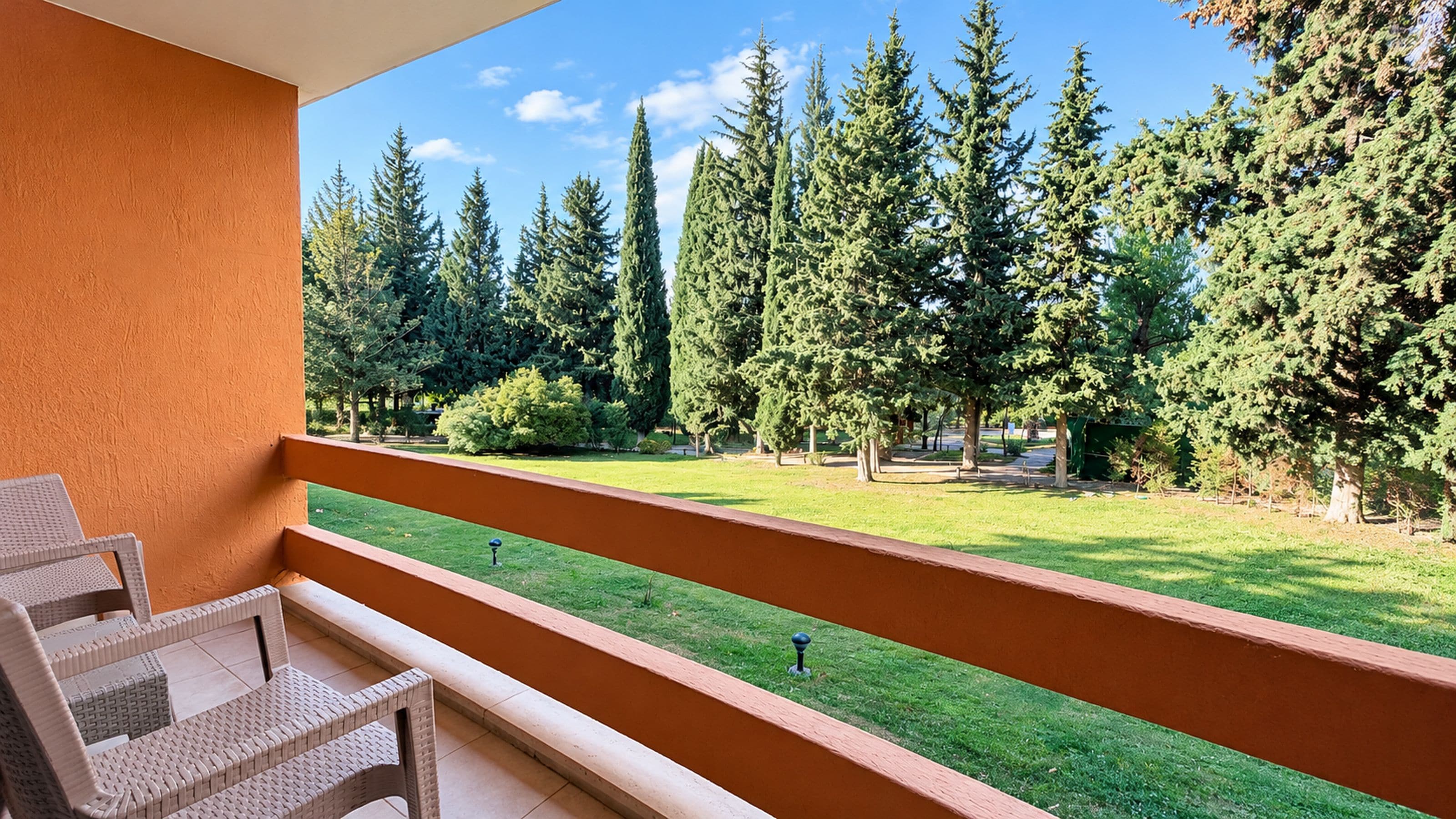A balcony with a view of a well-maintained lawn and tall trees.