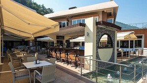 An outdoor seating area with tables and chairs, a pool, and a building with a tiled facade. - Balcova Thermal Hotel (Izmir)