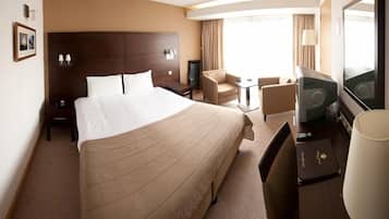 A hotel room with a large bed, a desk with a chair, a television, and a lamp.