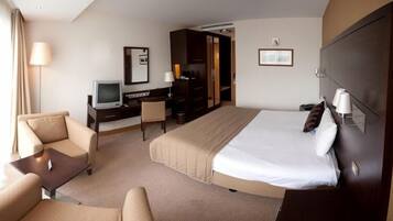A hotel room with a bed, a desk, a chair, a television, and a lamp.