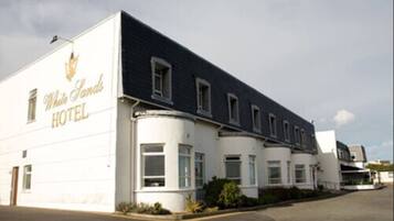 A hotel with a white facade and a dark roof, featuring a sign that reads "White Sands Hotel".