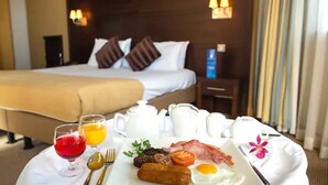 Una camera d'albergo con un letto rifatto, un comodino con una lampada e un vassoio per la colazione con uova, pancetta, salsiccia e un bicchiere di succo d'arancia.