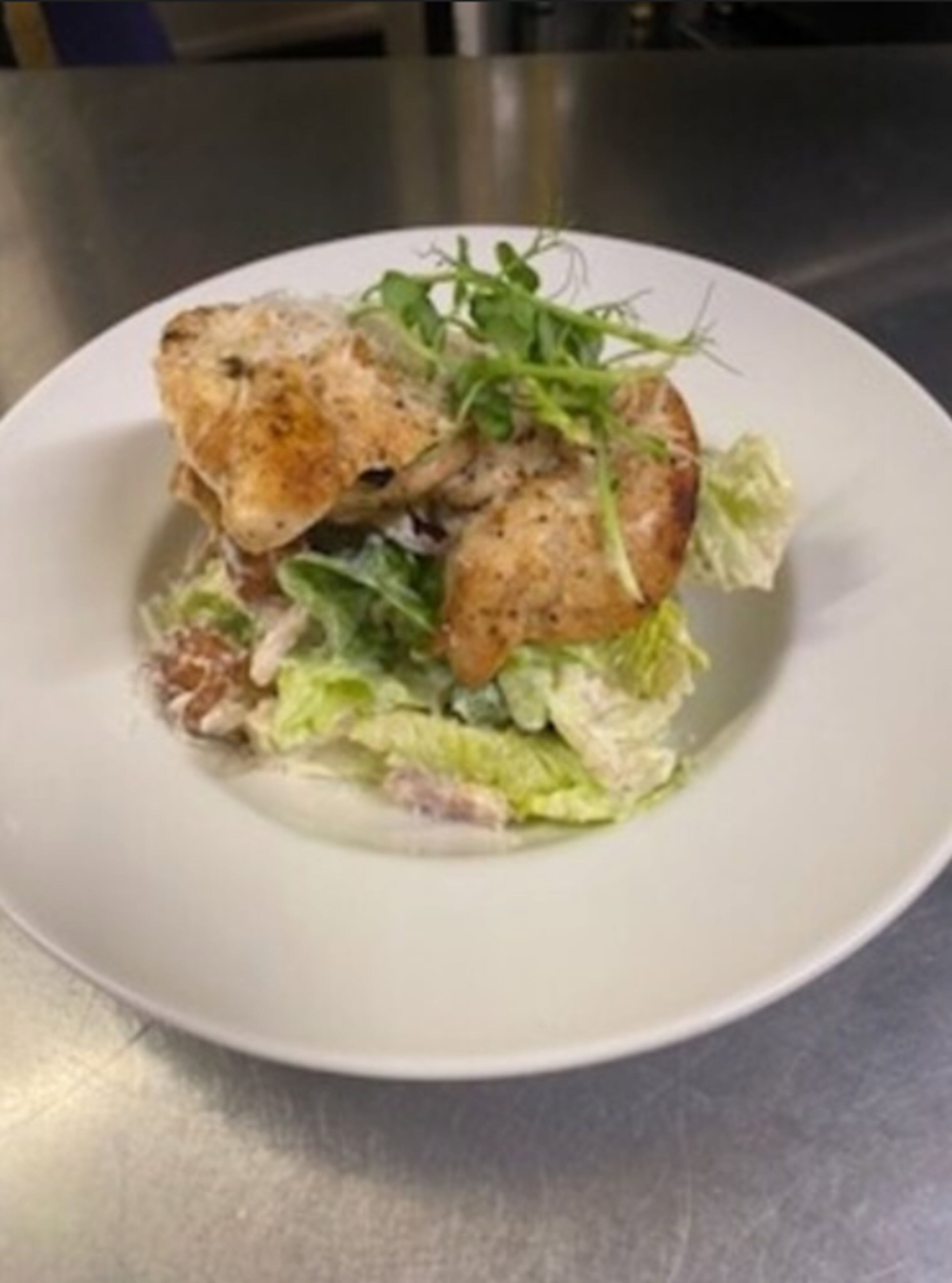A plate with a chicken sandwich, lettuce, and a garnish on a white plate.
