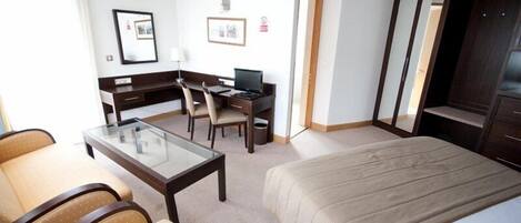 Ein Hotelzimmer mit Bett, Schreibtisch, Computer, Sessel und einer Couch.