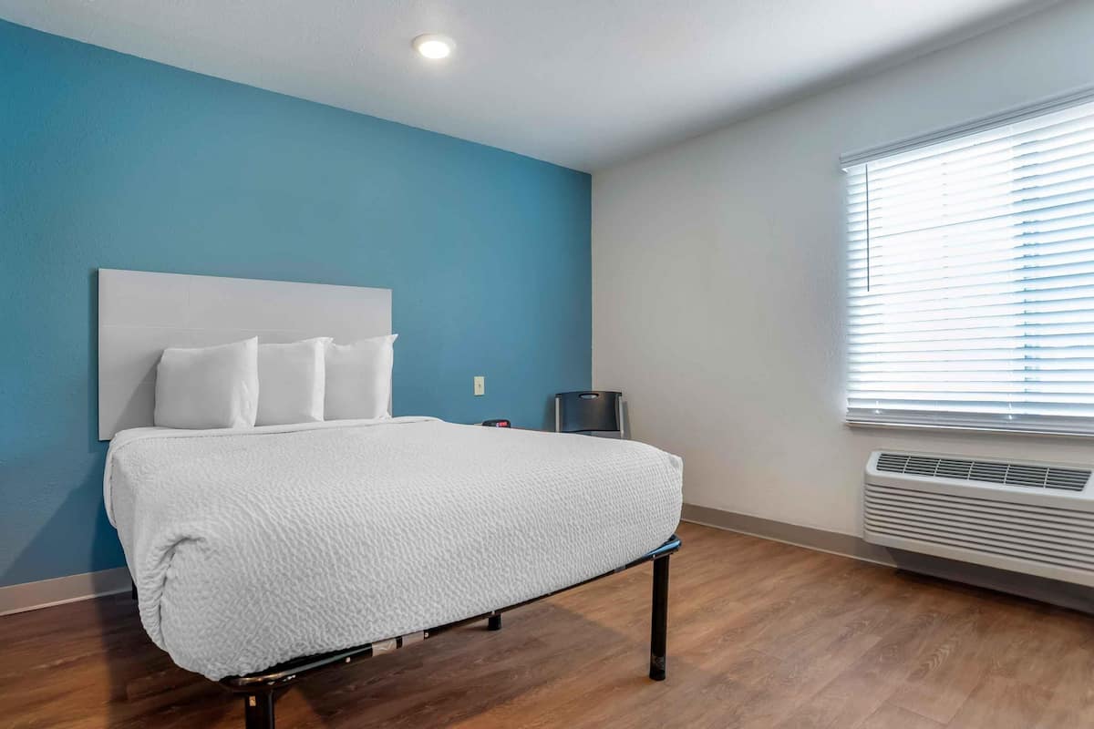 A hotel room with a bed, a wall heater, and a window with blinds.