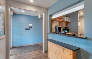 Un espace d’accueil avec un comptoir en bois, un ordinateur et une étagère contenant divers objets.