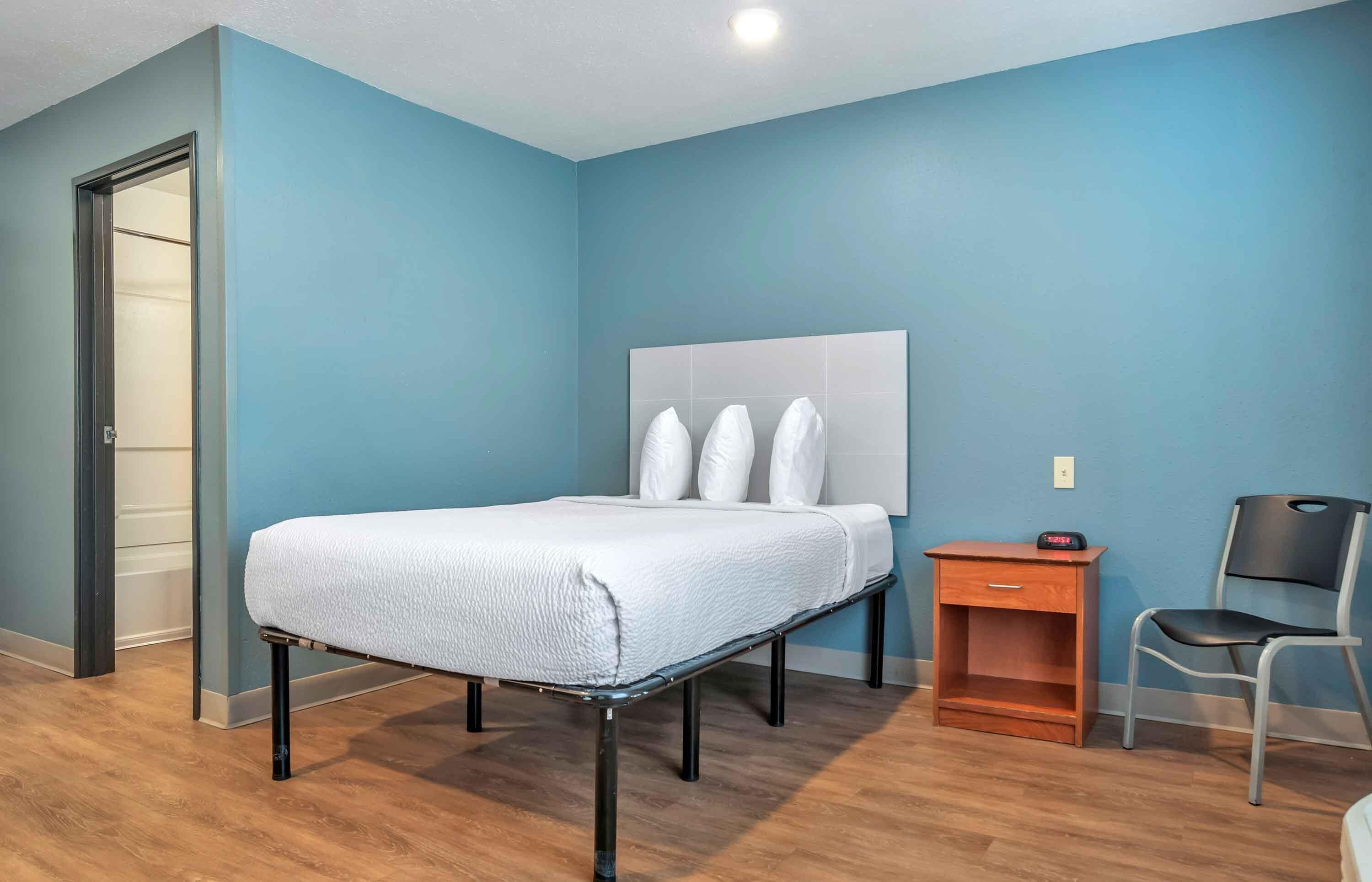 Ein Zimmer mit einem Bett, einem Nachttisch, einem Stuhl und einer Tür.
