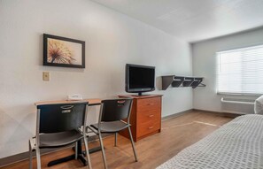 A hotel room with a desk, two chairs, a television, a dresser, and a bed.