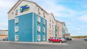 Un hotel con fachada azul y beige, varios pisos y un estacionamiento con varios coches.