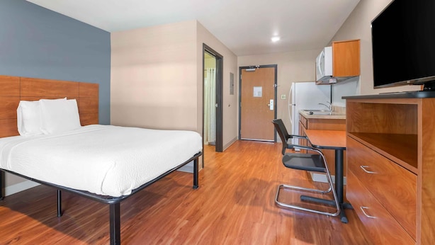 Una habitación de hotel con una cama, un escritorio con una silla, un televisor y una kitchenette.