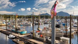 A marina with boats docked at wooden piers, a flagpole with a flag, and mountains in the background. - The Inn at Creek Street (Ketchikan)