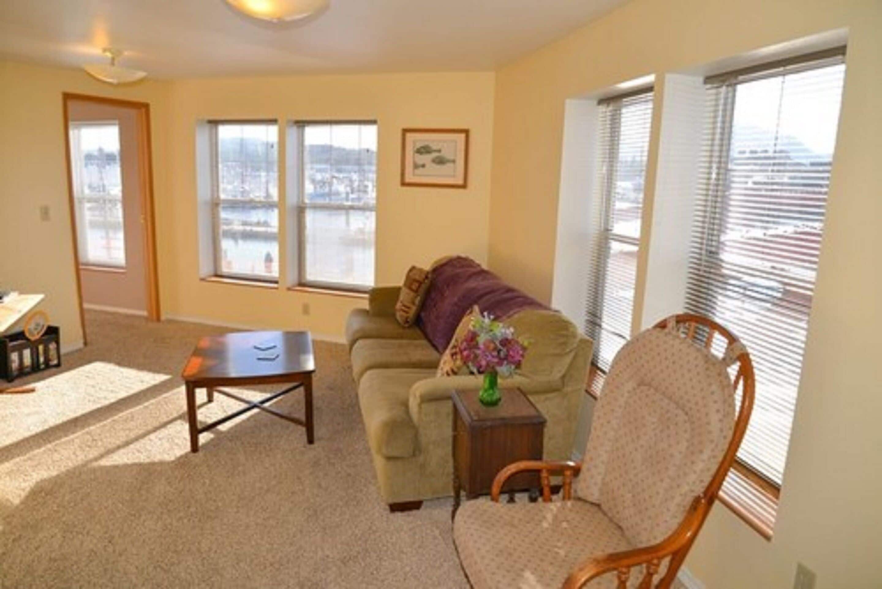 A living room with a sofa, a chair, a small table, and a view of a body of water through large windows.