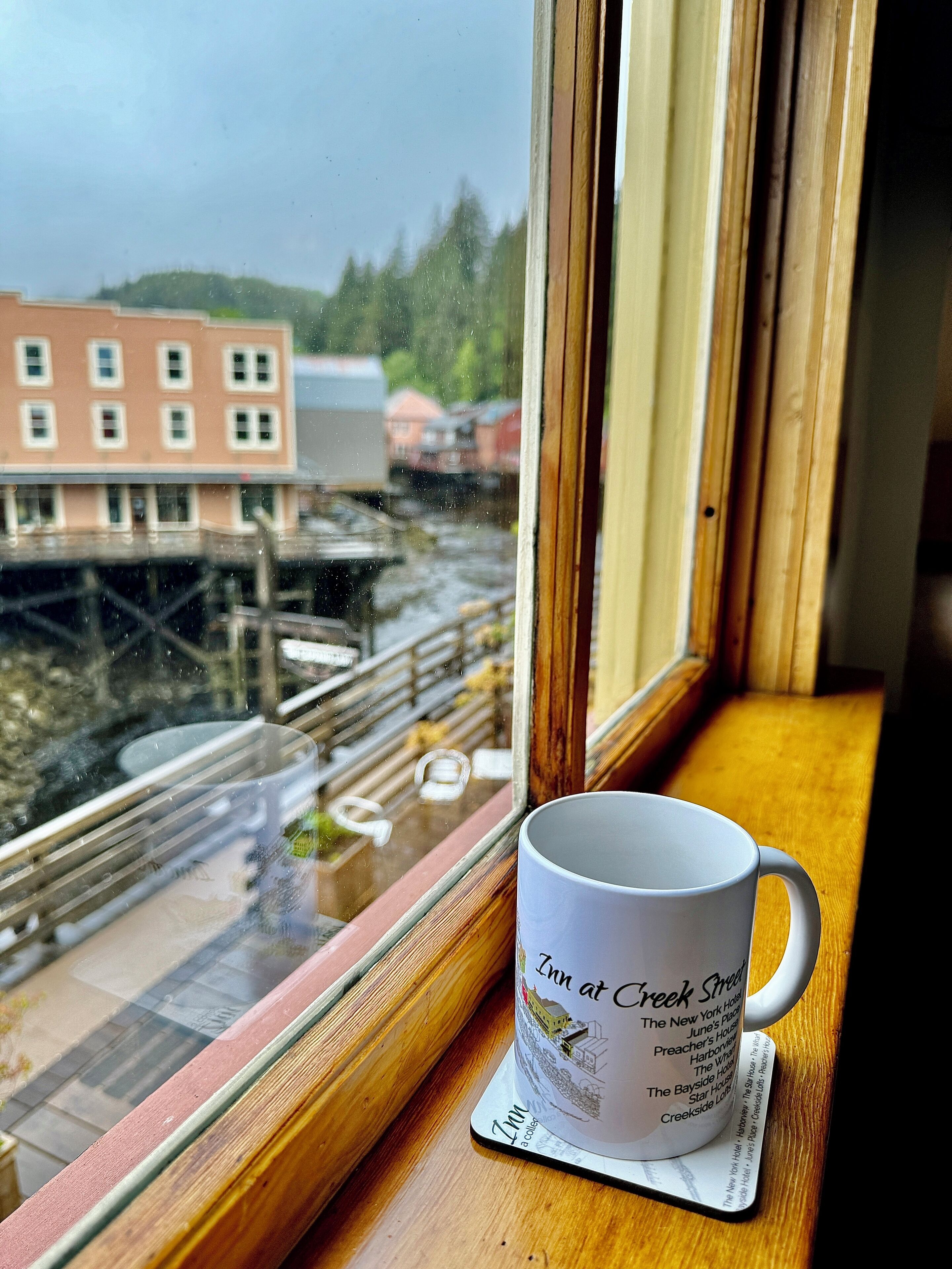 Une tasse blanche avec l’inscription « Inn at Creek Street », posée sur un dessous de verre, elle-même placée sur une étagère en bois près d’une fenêtre.