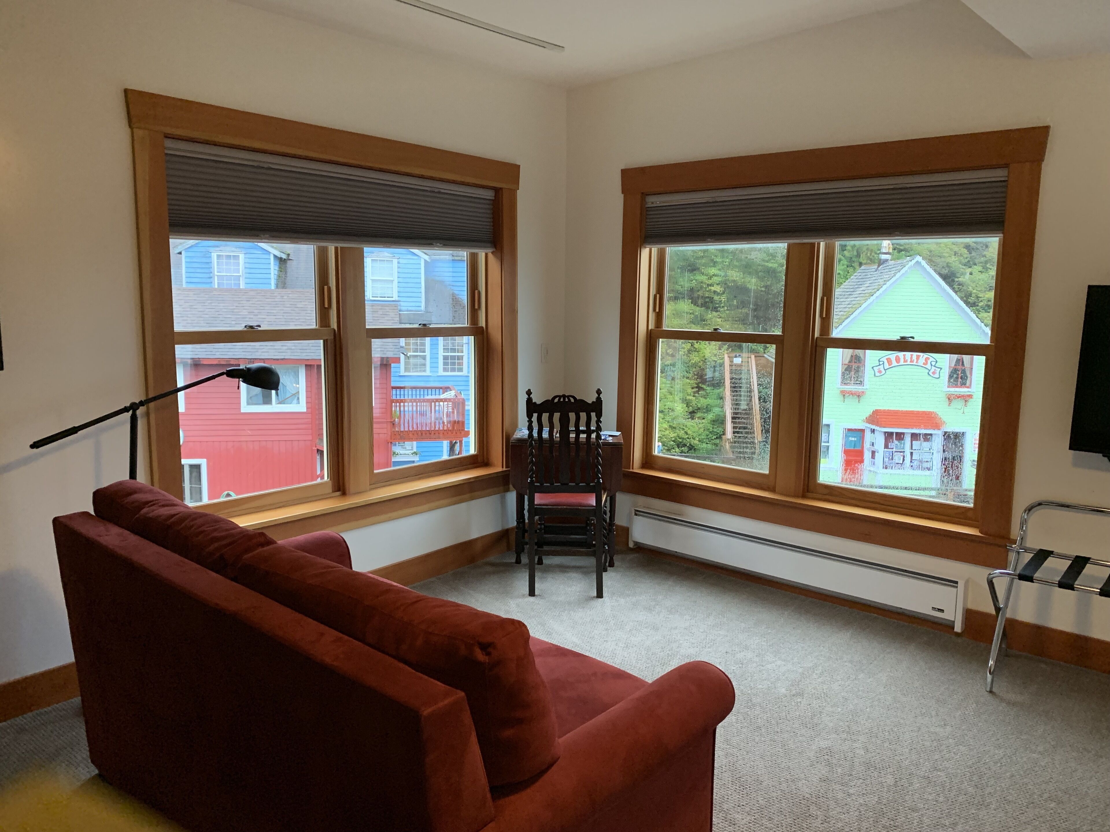 A room with a red sofa, a wooden chair, and large windows with blinds.