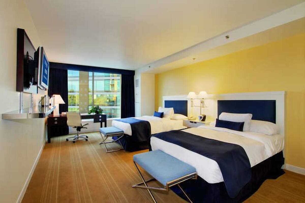 A hotel room with two beds, a desk, a chair, and a large window.