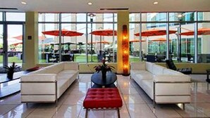 A modern lobby with white sofas, a red ottoman, and large windows with red umbrellas.
