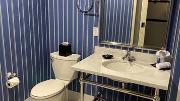 A bathroom with a striped blue and white wall, a white toilet, a sink with a mirror, and a towel rack with towels.