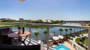 A balcony with a view of a lake, outdoor seating, and a swimming pool.