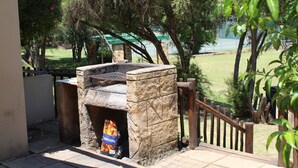 Een buitengebied met een barbecue, een stenen grill, een zak kolen en een houten omheining.