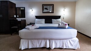 Een groot, net opgemaakt bed met witte lakens en een blauw accent, een donker hoofdbord en twee wandlampen.