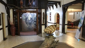 Een lobby met een houten sculptuur, een glazen tafel met een decoratief object en een groot stuk boomstam als middelpunt.