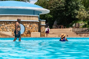 A swimming pool with a stone wall and a blue roof structure. - Gooderson Natal Spa Hot Springs & Leisure Resort (Paulpietersburg)