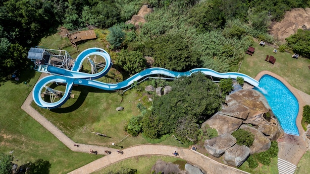 Een waterglijbaan met een zwembad aan het einde, omringd door groen en rotsen.