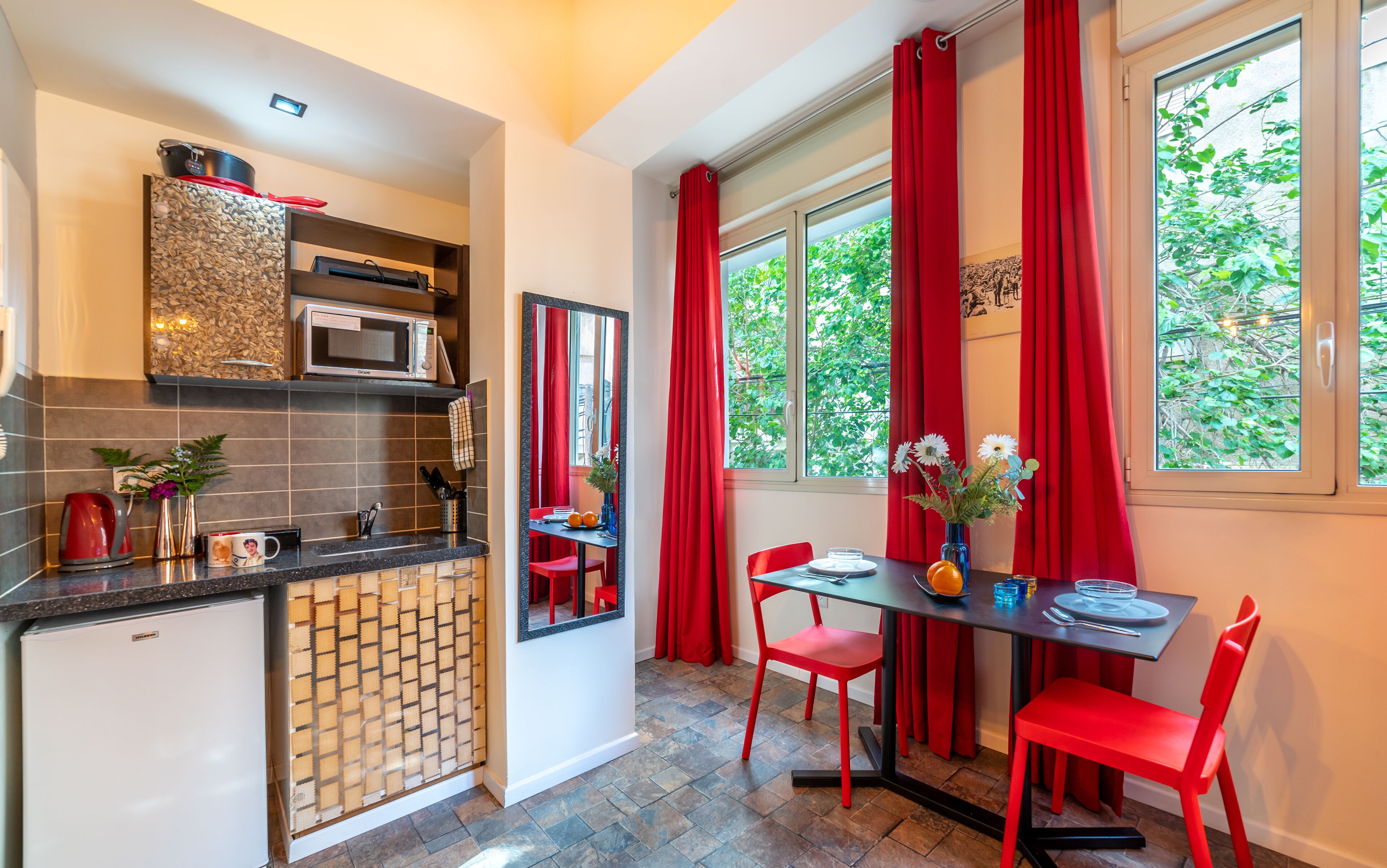 A modern kitchen with a microwave, kettle, and red chairs at a dining table.