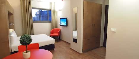 Une chambre d’hôtel comprenant un lit, une télévision, un bureau avec une chaise, une petite plante et une armoire.