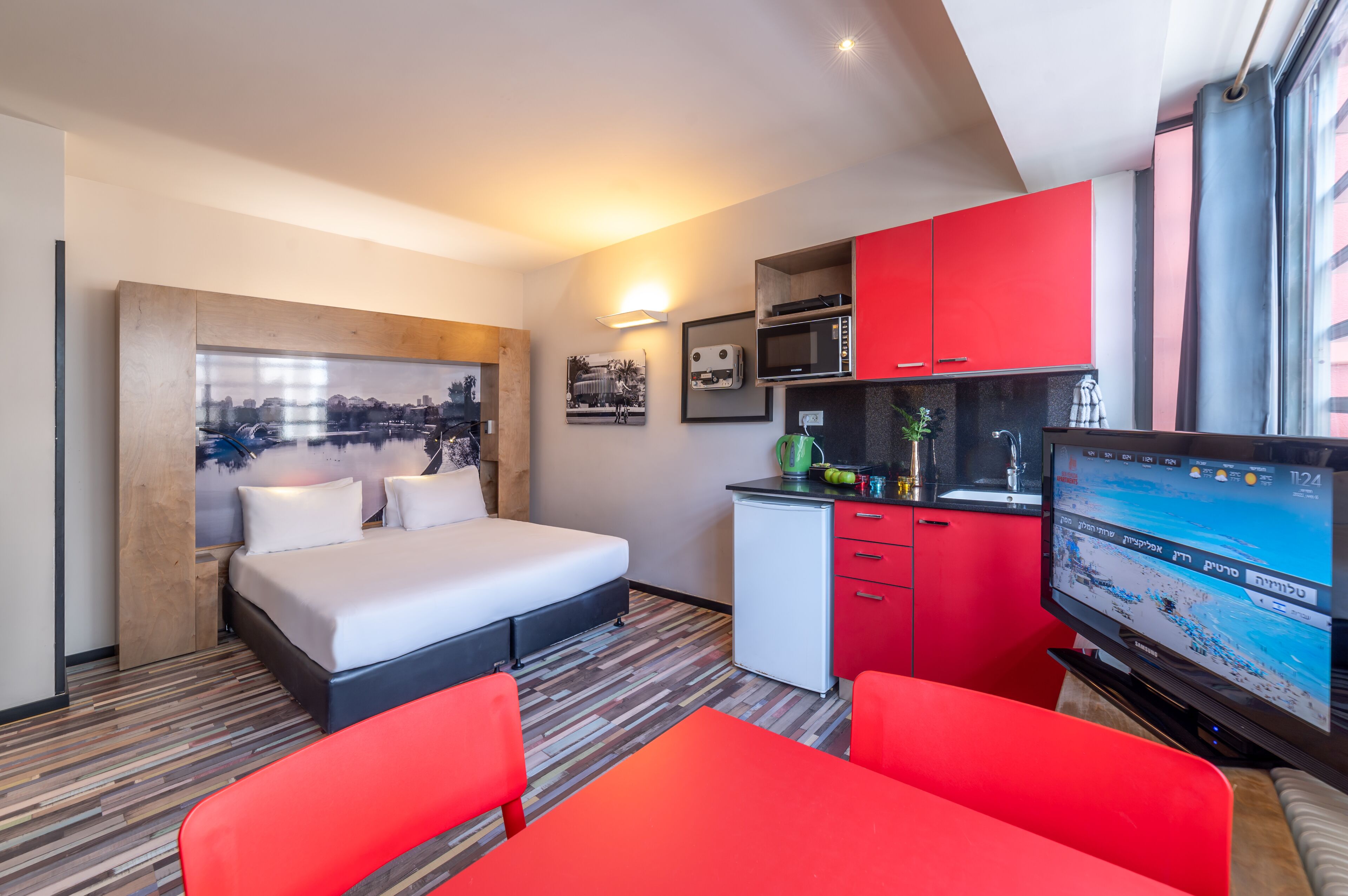 Una habitación de hotel compacta con una cama, una kitchenette pequeña, un televisor y una silla roja.