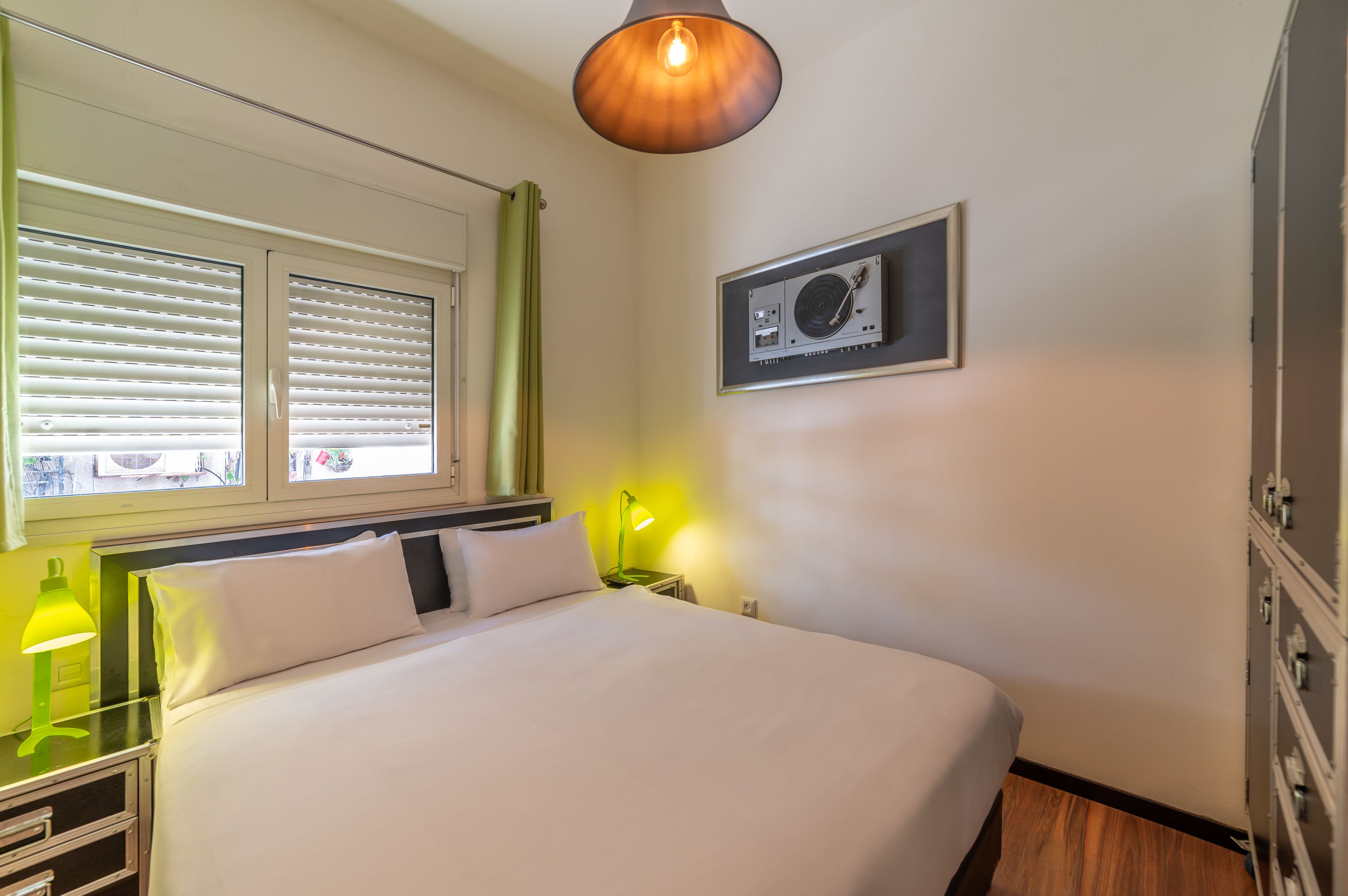 Hotelkamer met een bed, een raam met zonwering, een wandairconditioner en een groene lamp.