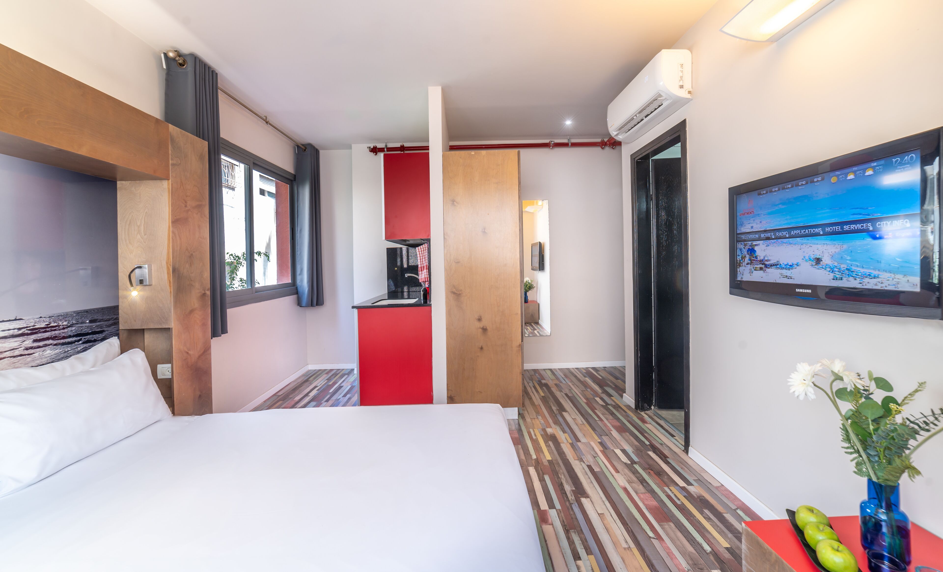 Une chambre d’hôtel avec un lit, une télévision, un plancher en bois et un mur d’accent rouge.