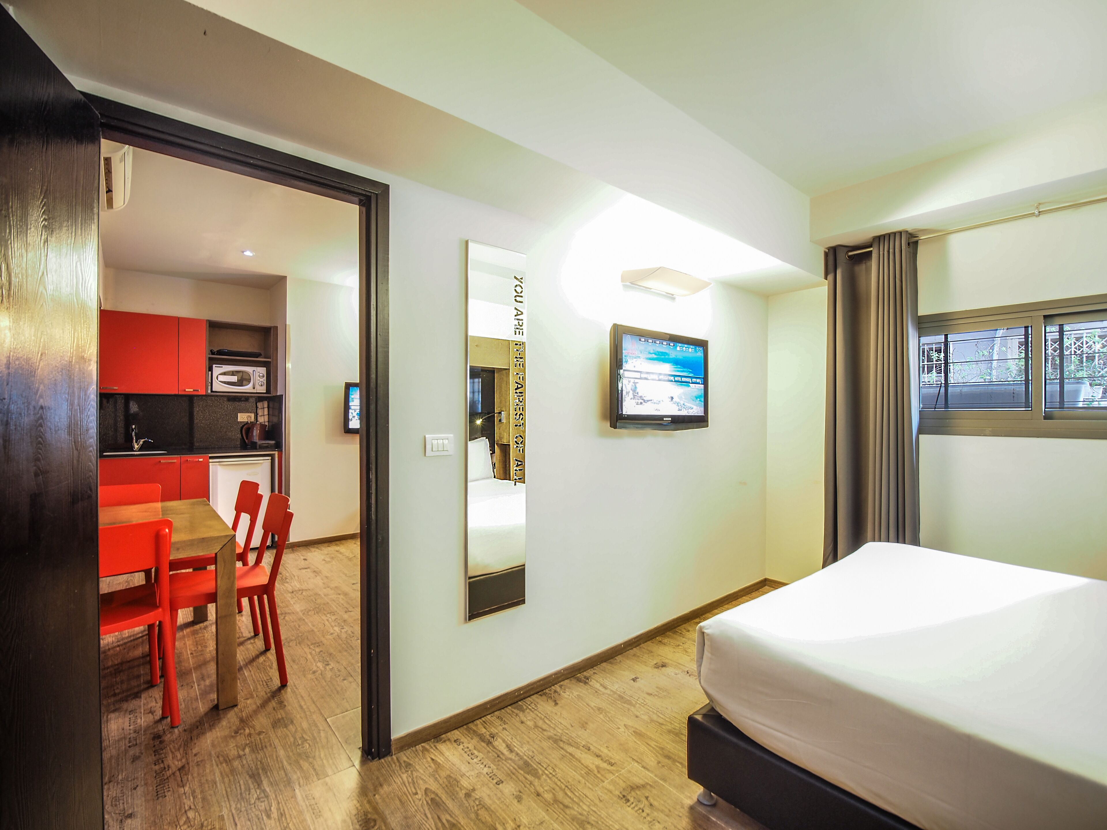 A hotel room with a bed, a TV, a desk with a chair, and a kitchenette.