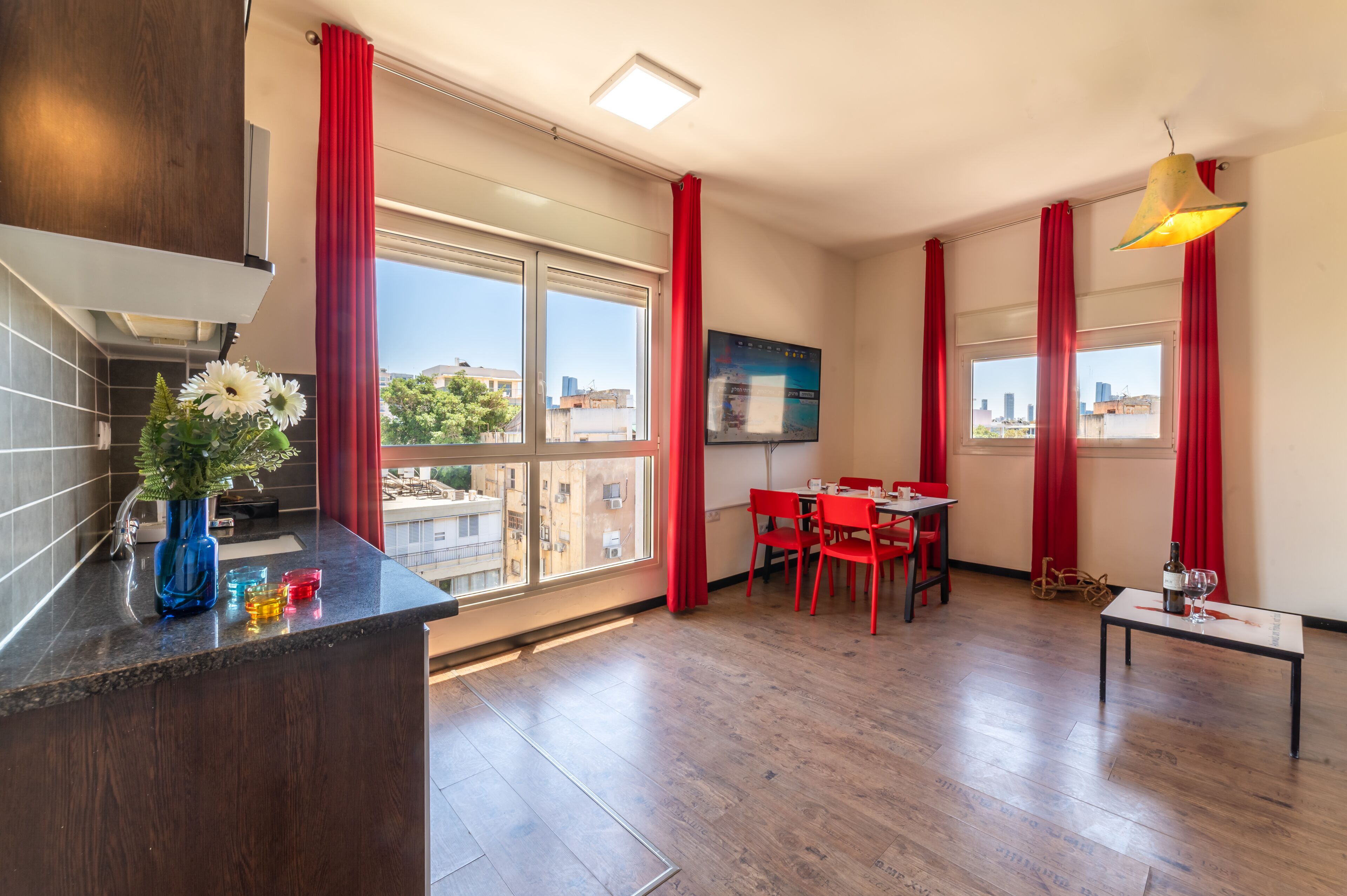 Een moderne kamer met een keukenhoek, eettafel en grote ramen met rode gordijnen.