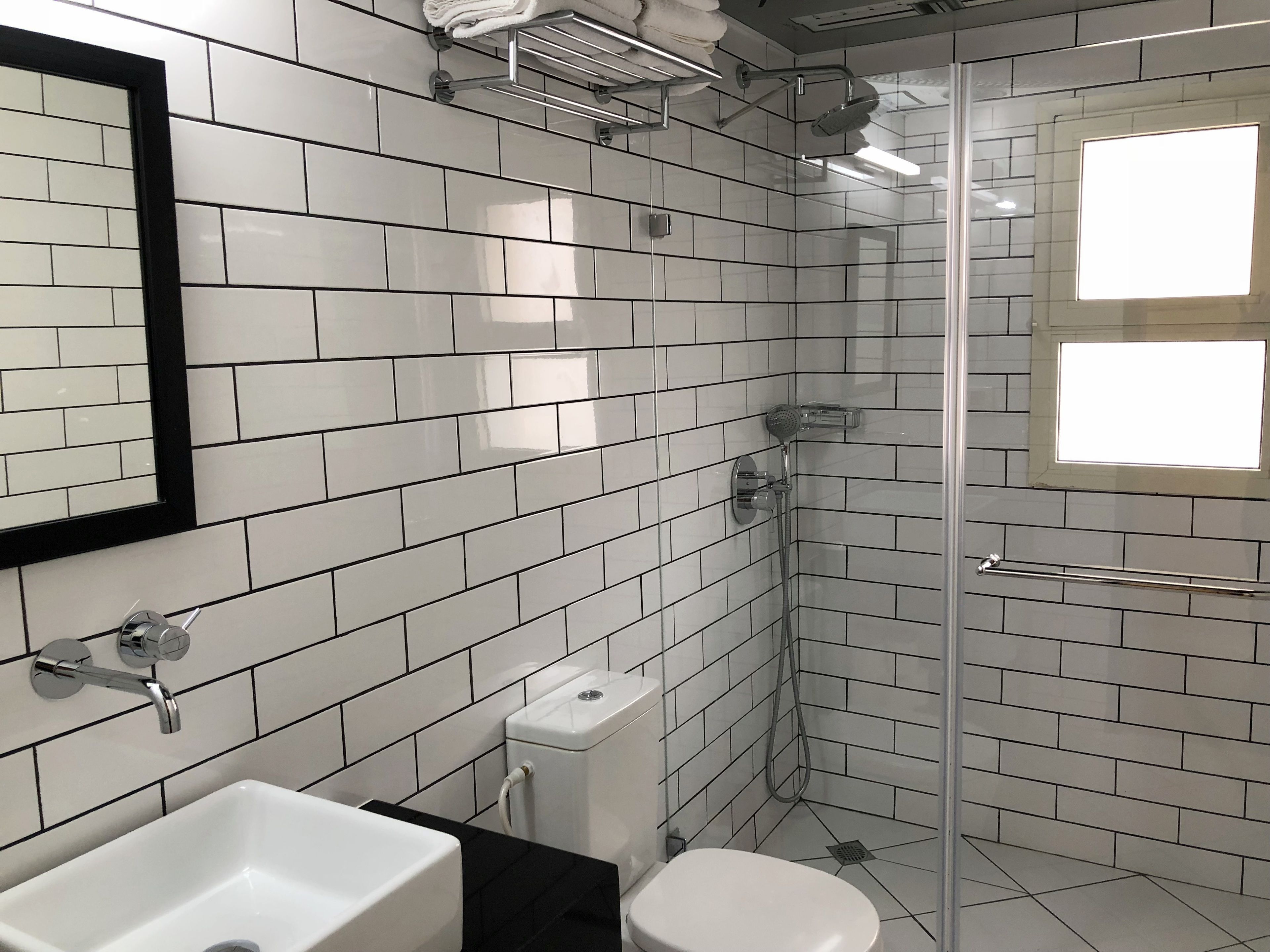 Een badkamer met witte metrotegels, een witte wastafel, een toilet en een douche met glazen deur.